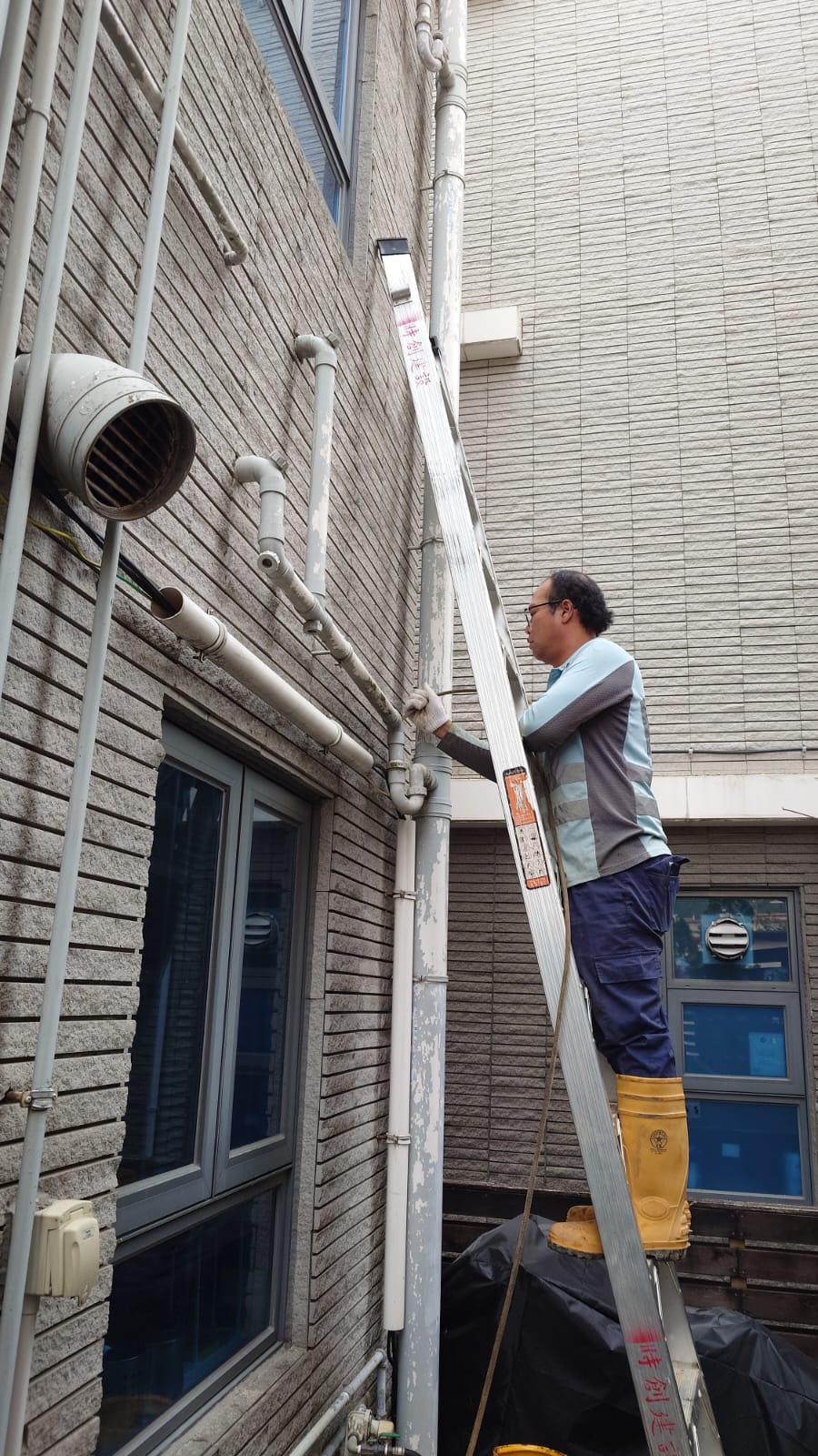 Technician clearing an exterior drain pipe on a ladder